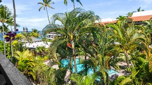A tropical resort with a pool surrounded by palm trees and a view of the ocean. - Big Island Casa De Emdeko A308 1 Bedroom Condo (Kailua-Kona)