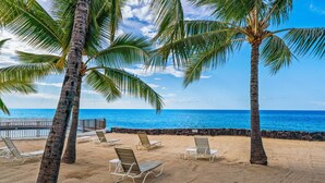 A beach with palm trees, lounge chairs, and a view of the ocean. - Big Island Casa De Emdeko A308 1 Bedroom Condo (Kailua-Kona)
