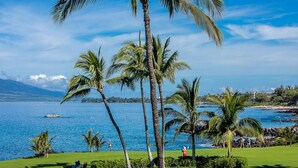 A tropical landscape with palm trees, a golf course, and a view of the ocean. - Kihei Surfside 412 1 Bedroom Condo (Kihei)