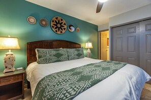 A bedroom with a bed, two bedside tables with lamps, a wooden headboard, and decorative wall art. - Kihei Surfside 412 1 Bedroom Condo (Kihei)