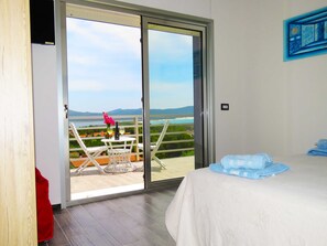 A bedroom with a large sliding glass door leading to a balcony with a view of a body of water and mountains. - Apartment with a breathtaking view of Portopino Bay (Porto Pino)