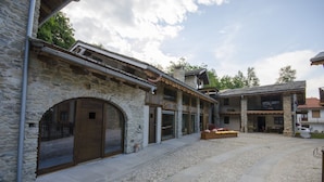 Un edificio de piedra con puerta de madera y ventanas grandes, un patio de grava y un banco de madera con flores.
