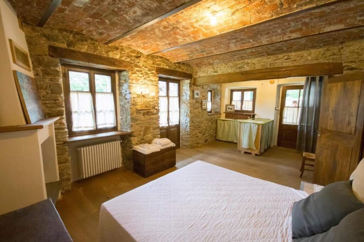 A rustic room with a stone wall, a bed, a wooden bench, and a small table.