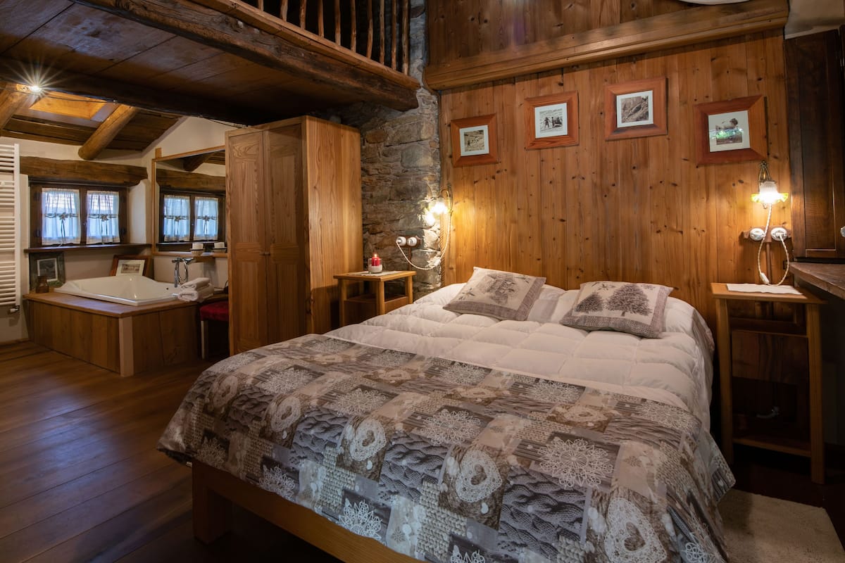 A wooden room with a large bed, a wooden desk, and a stone wall.
