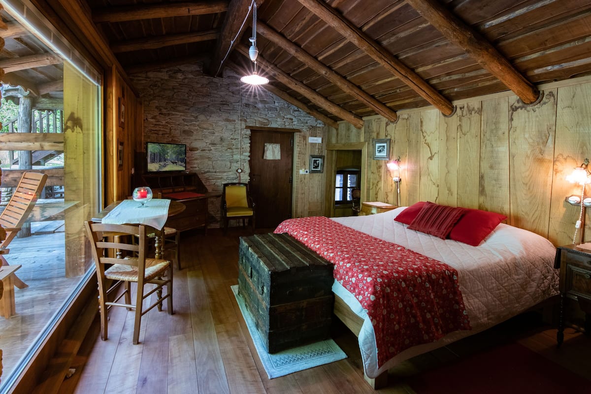 A rustic wooden room with a bed, a desk, and a stone wall.