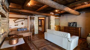 Ein rustikales Interieur mit freiliegenden Holzbalken, Steinwänden, einem weißen Sofa, einem Holztisch mit einem Topf und einem Schmuckkästchen mit einem Bild.