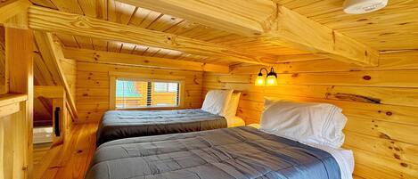 Eine Holzhütte mit zwei Betten, Holzvertäfelung, einem Fenster und einer Deckenleuchte.
