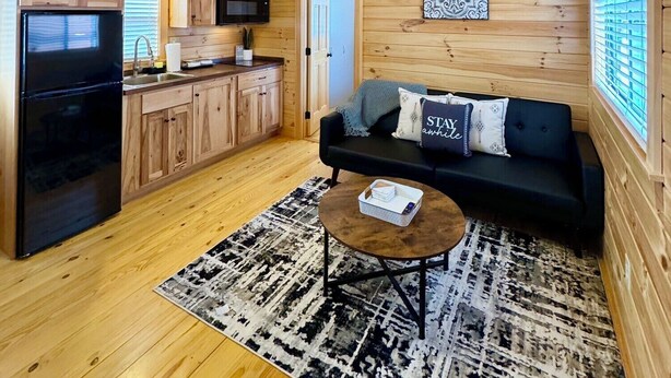 A wooden cabin interior with a kitchen, a black sofa, and a ceiling fan. - Walking Distance to Lakes James with Resort Amenities (Marion)
