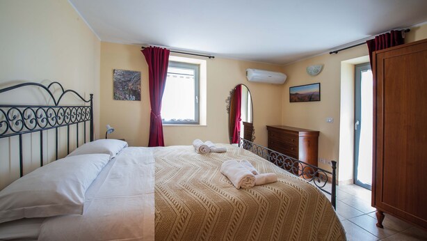 A bedroom with a bed, a wooden wardrobe, a window with curtains, and a wall-mounted air conditioner.