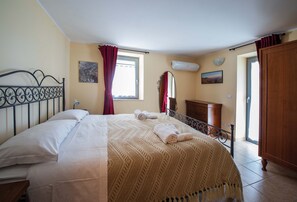 A bedroom with a bed, a wooden wardrobe, a window with curtains, and a wall-mounted air conditioner. - Guardea, apartment to reach Orvieto in 20 minutes (Guardea)