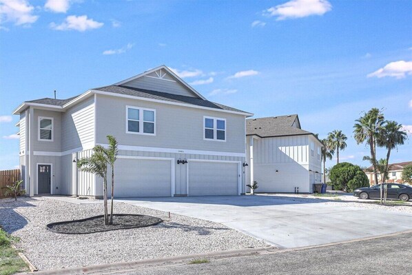 A two-story house with a garage, a driveway, and a small garden area. - North Padre Island Roomy Beach House Unit B (Corpus Christi)