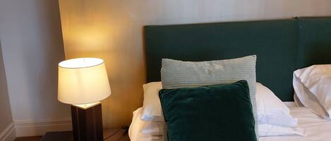 A neatly made bed with white linens and a green pillow, a bedside table with a lamp, and a framed picture of animals on the wall.
