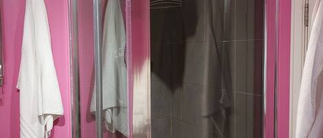 A glass-enclosed shower with a white bathtub, pink walls, and a white towel hanging on the wall.