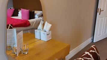 Habitación de hotel con una mesa de madera, un espejo, una cama con almohadas rosas y marrones, y una puerta.