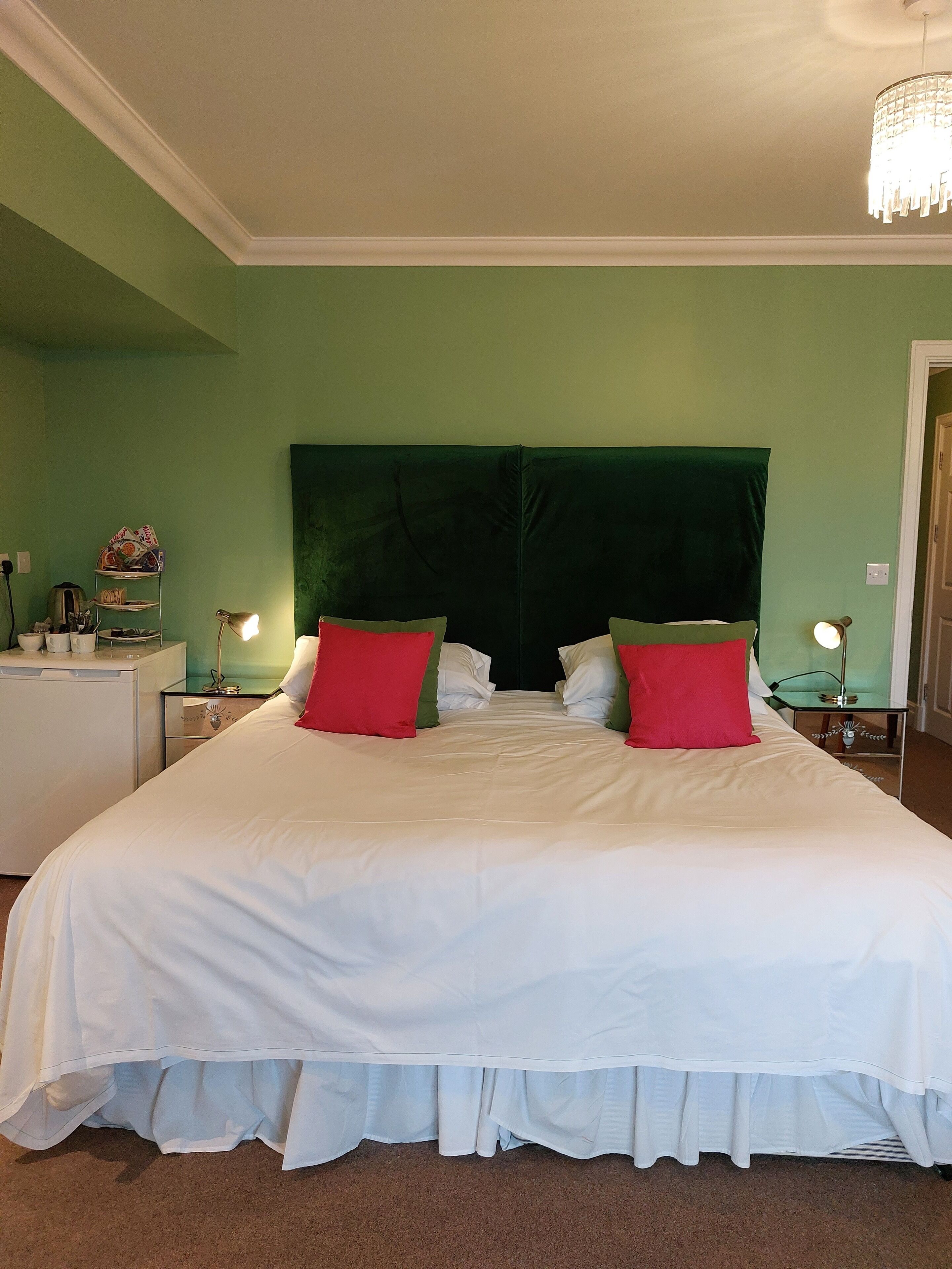A neatly made bed with white bedding and red pillows, a green headboard, and bedside tables with lamps.