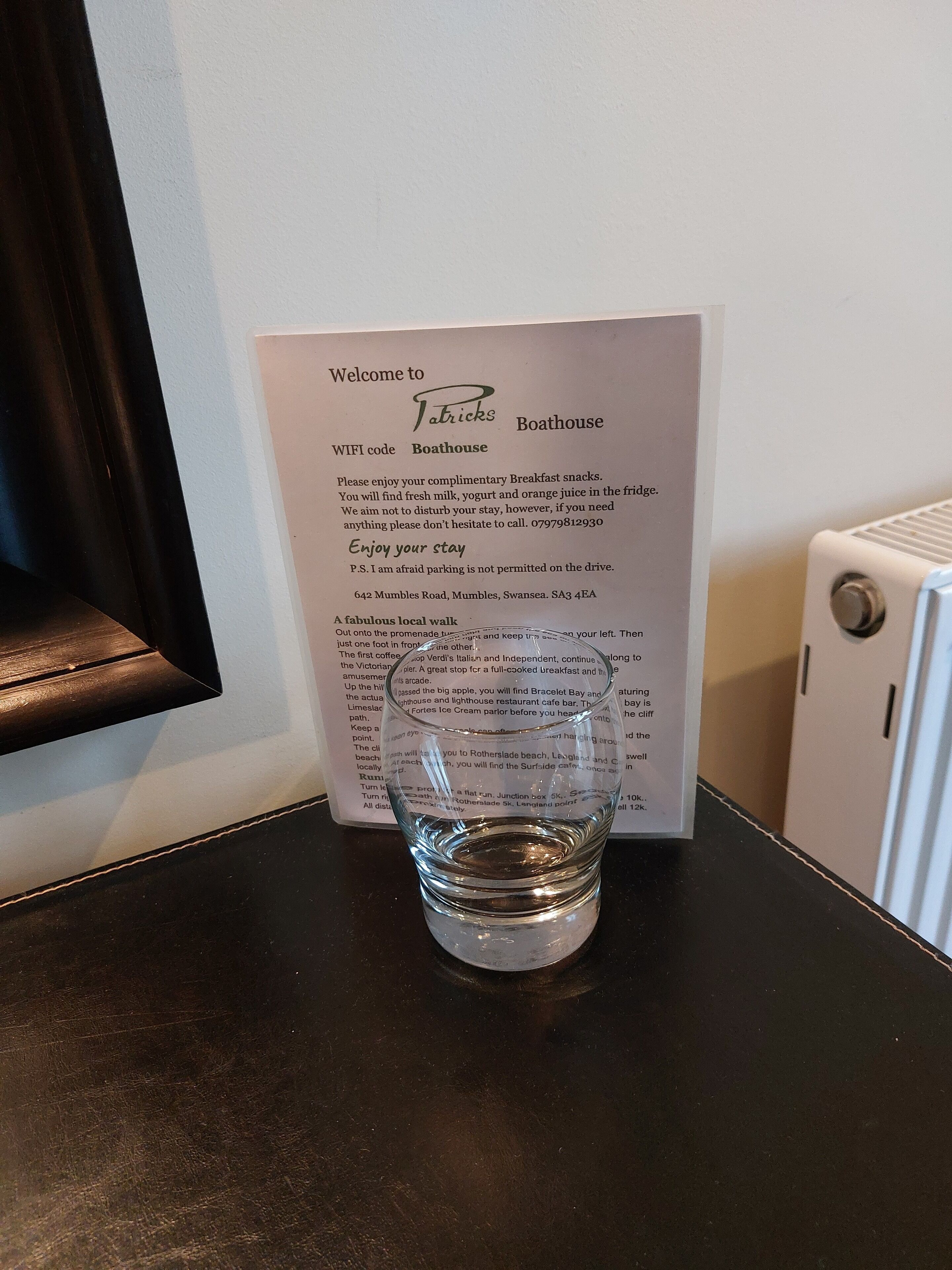 A glass of water on a black table with a welcome sign for 'Patrick's Boathouse' behind it.