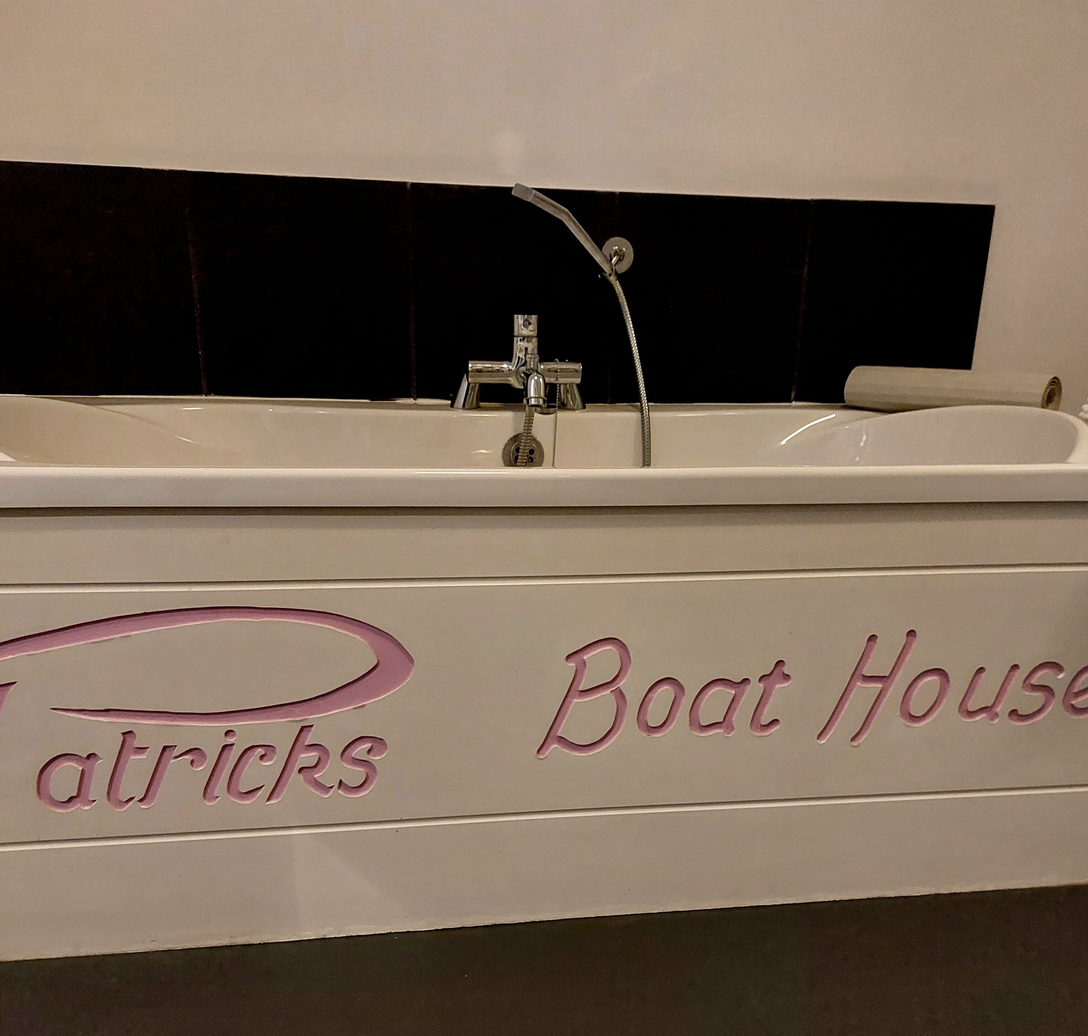 Un baño con un lavamanos blanco, un espejo y un perchero para toallas. En la pared hay un letrero que dice "Boat House".