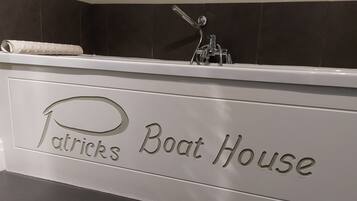 Un baño con bañera, una toalla y cabezal de ducha. La pared presenta un diseño de azulejos oscuros y un cartel que dice "Patrick's Boat House".