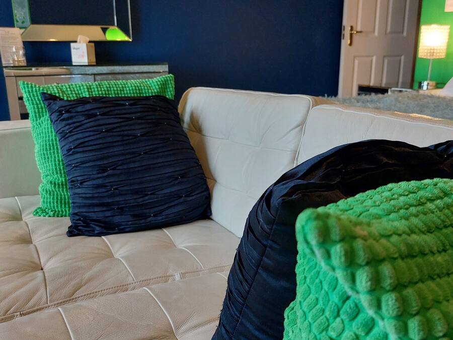 Quarto com sofá bege, almofadas verdes e pretas, um espelho e parede verde.