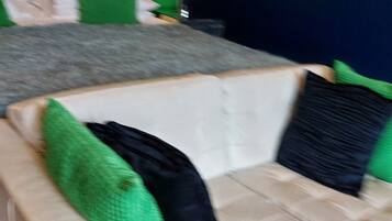 A room with a white sofa, green and black pillows, a bed with a white headboard, and a green wall.