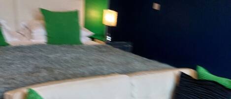 Una habitación con un sofá blanco, almohadas verdes y negras, una cama con cabecera blanca y una pared verde.