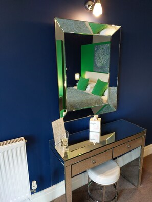 A bathroom with a large mirror, a vanity with a glass top, a white radiator, and a stool.