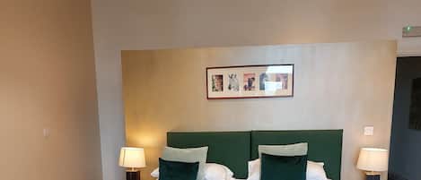 A hotel room with a large bed, two bedside tables, a grey sofa with green cushions, and a wooden coffee table.