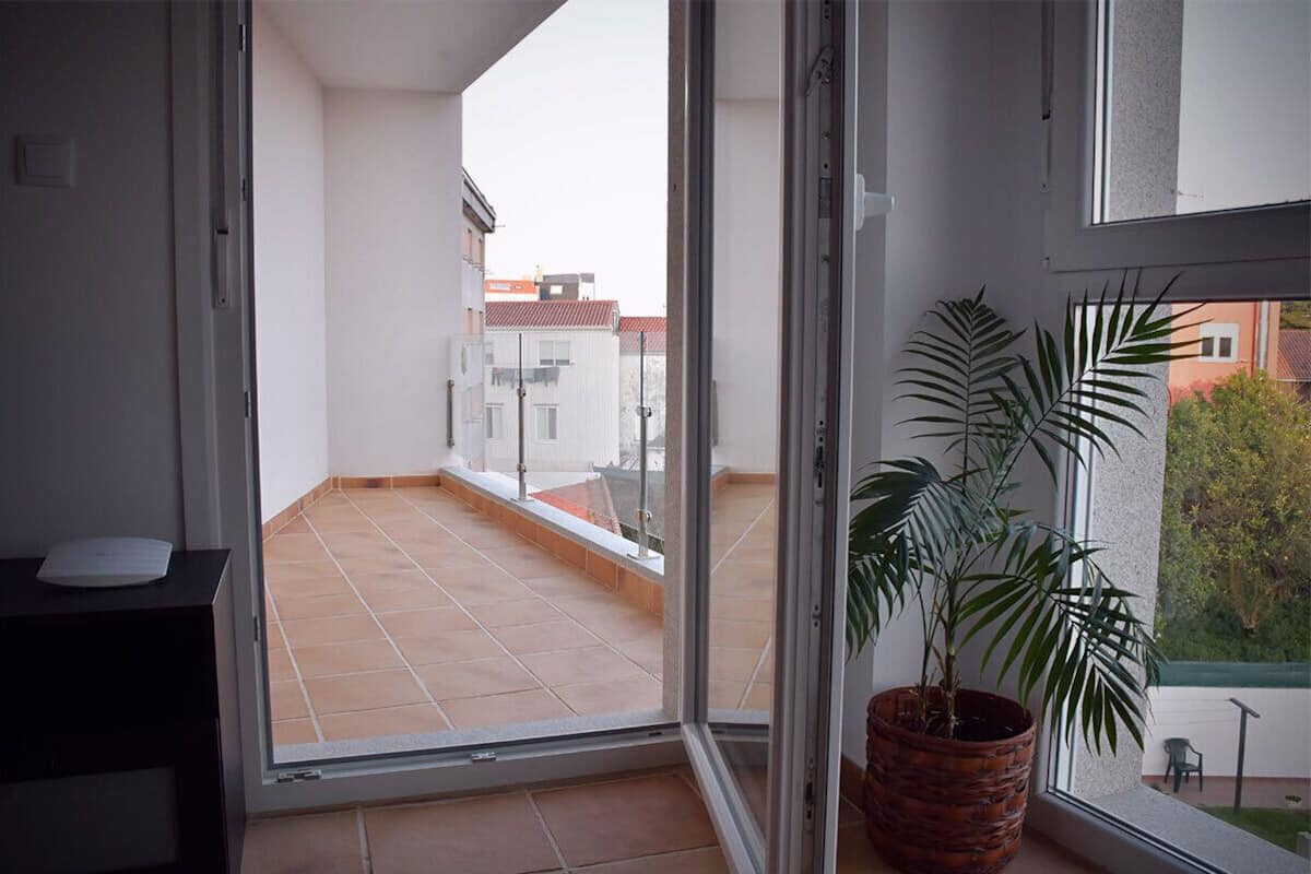 Een balkon met een bloempot, een schuifdeur en uitzicht op gebouwen.