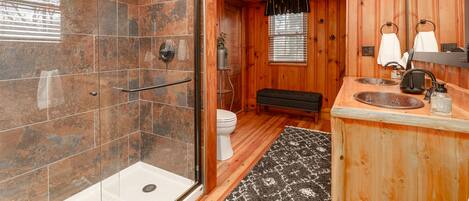 A bathroom with a glass shower enclosure, wooden walls, a toilet, a bench, and a sink with a mirror.