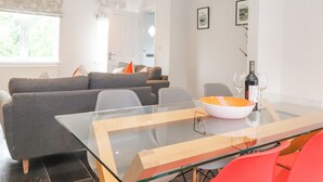 A modern living room with a glass dining table, grey sofas, and a red chair. - 1 Millbank (Keswick)