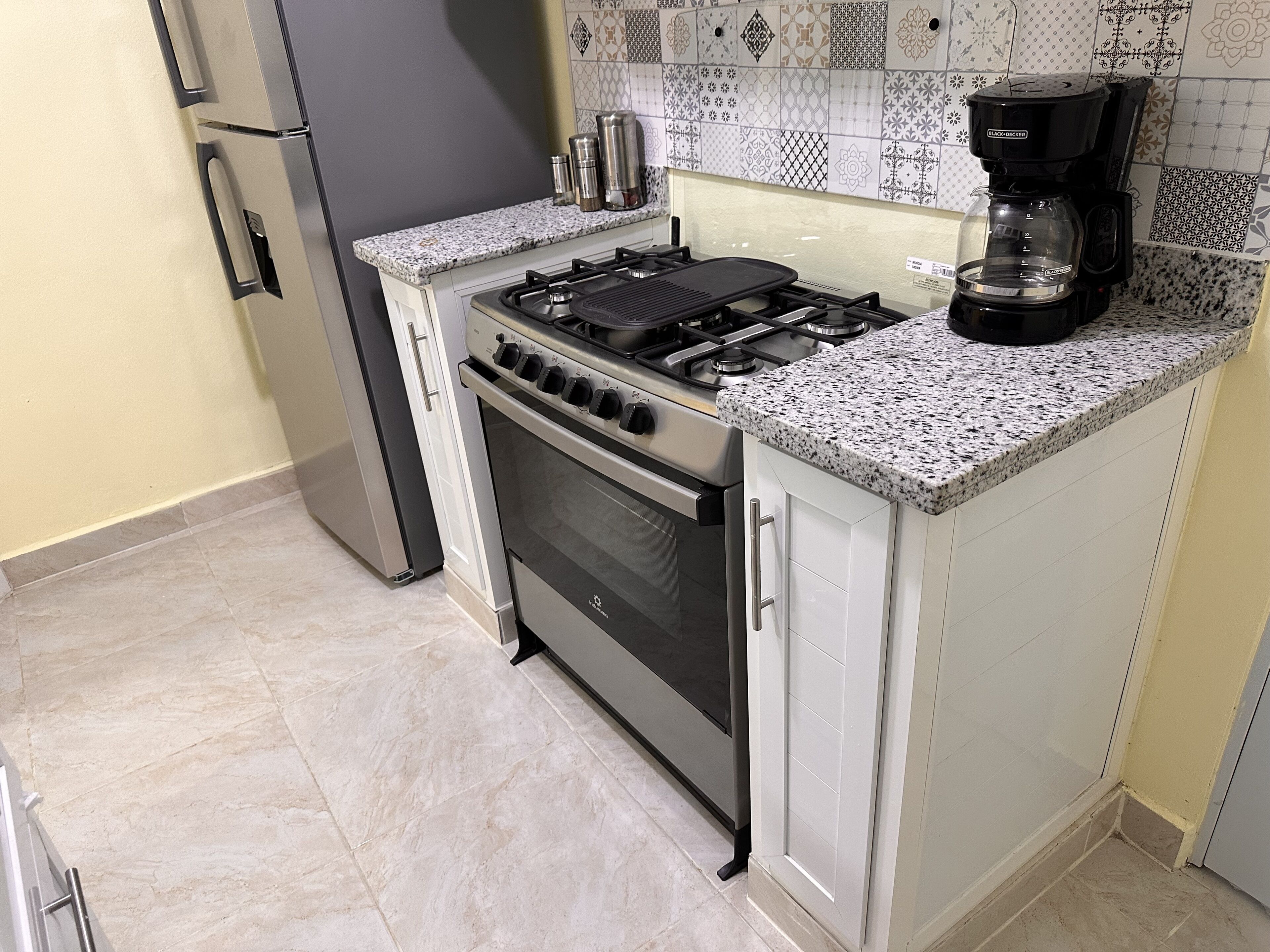 Eine Küche mit Gasherd, Backofen, Kühlschrank und Kaffeemaschine.