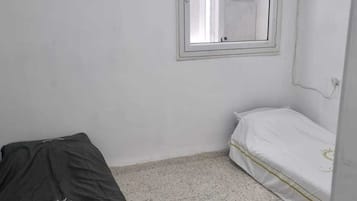 Una habitación pequeña y poco amueblada, con una cama, un ventanal y un aire acondicionado.