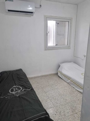Una habitación pequeña y poco amueblada, con una cama, un ventanal y un aire acondicionado.