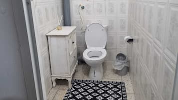 Un baño pequeño con inodoro, un armario, una ventana y un tapete estampado.