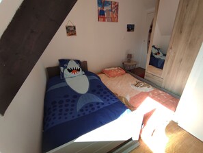 A bedroom with a bed featuring a shark-themed pillow, a small round table with a lamp, and a mirror on the wall. - Les Petits Embruns, Moins de 2 km des Plages (Moëlan-sur-Mer)