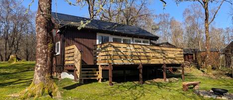 A wooden cabin with a deck, surrounded by trees and grass.