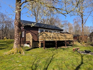 Une cabane en bois dotée d’une terrasse, entourée d’arbres et d’herbe.