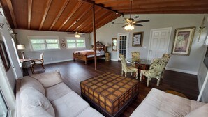 A spacious living room with a high ceiling, a large wooden ceiling fan, a cozy seating area with sofas, a round glass table surrounded by chairs, and a bed with a canopy. - Tropical Suite with Garden near Beaches & Nature in Melbourne (Melbourne)