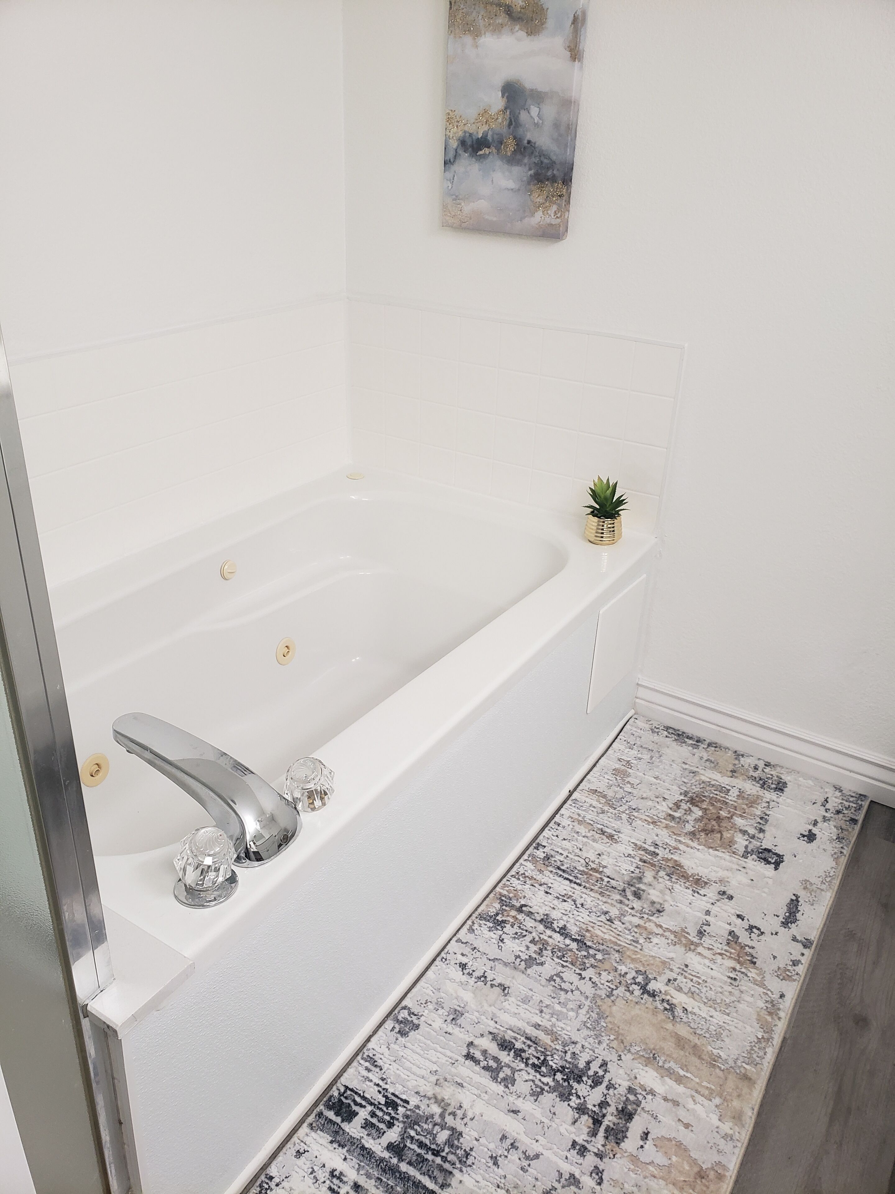 A modern bathroom with a white bathtub, a small potted plant, and a textured rug.