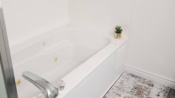 A modern bathroom with a white bathtub, a small potted plant, and a textured rug.