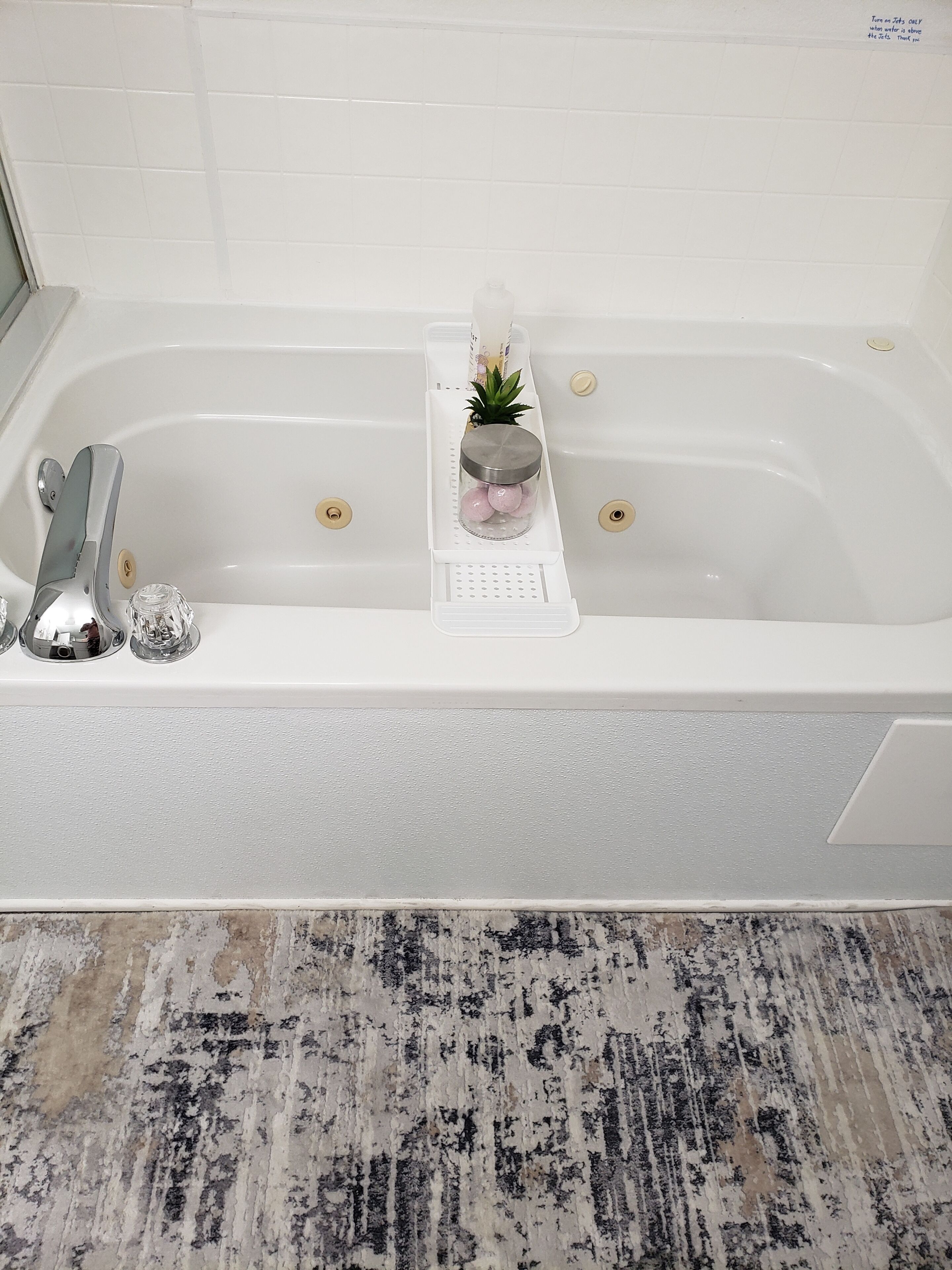 A white bathtub with a shelf holding a small plant and a glass jar.