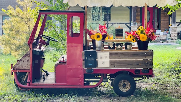 Un véhicule utilitaire rouge, équipé d’une cabine de protection et décoré de fleurs, est garé à l’extérieur.