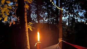 Un hamac tendu entre deux arbres, une bougie allumée et une chaise.
