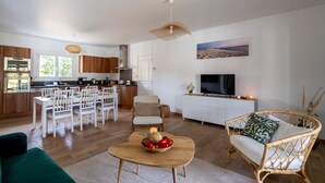 Ett modernt vardagsrum med en matplats, en soffa av rotting, en tv och ett kök i bakgrunden.