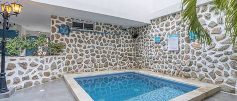 A swimming pool with stone walls and a tiled floor, surrounded by a well-maintained garden.