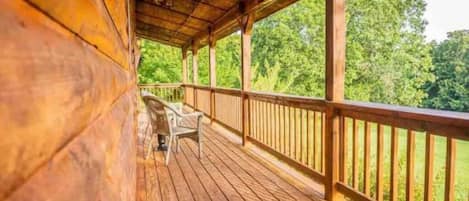A wooden deck with a railing, a chair, and a view of a forest.
