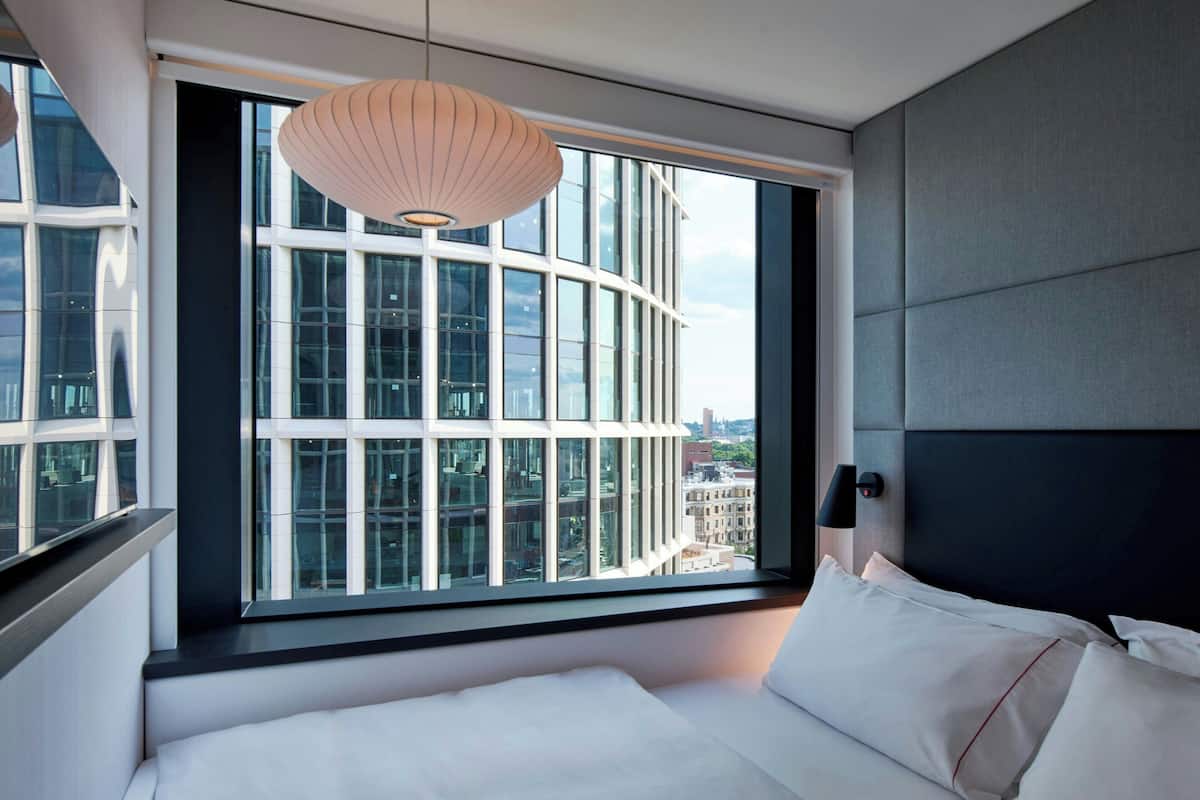 A modern hotel room with a large window, a bed, and a pendant light.