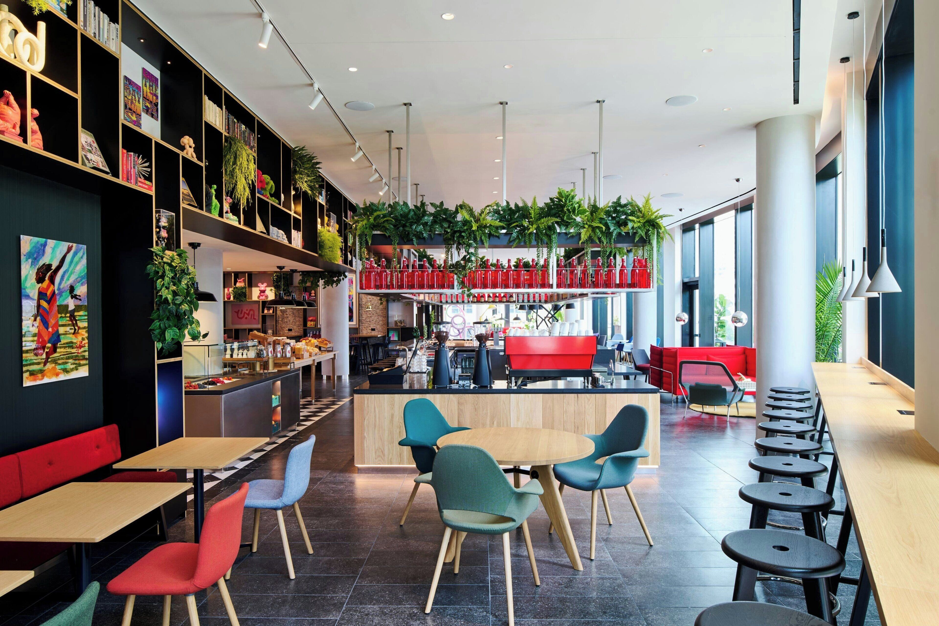 A modern restaurant with a central counter, multiple seating areas, and a variety of plants.