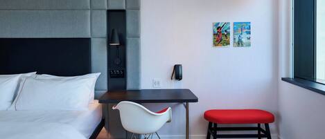 A modern hotel room with a bed, a desk, a chair, and a bench.
