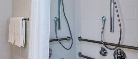 Un baño moderno con ducha envuelta en vidrio, bañera con barra de apoyo y pared de azulejos blancos.